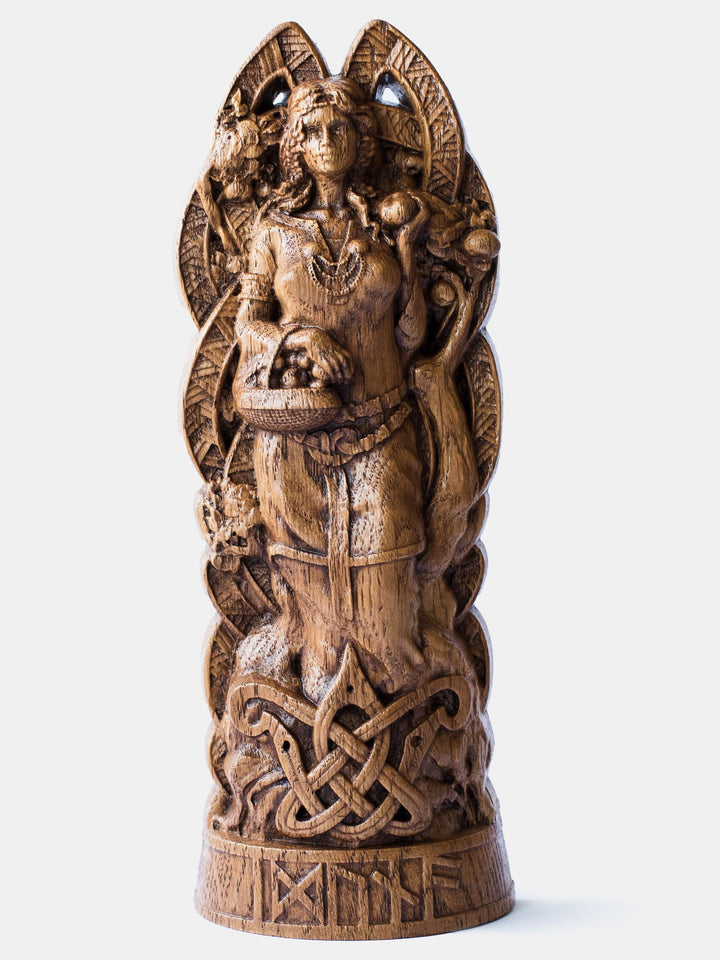 Close-up of the handcrafted oak Idunn statue, showcasing detailed carvings of Idunn holding a basket of golden apples with an apple tree in the background.