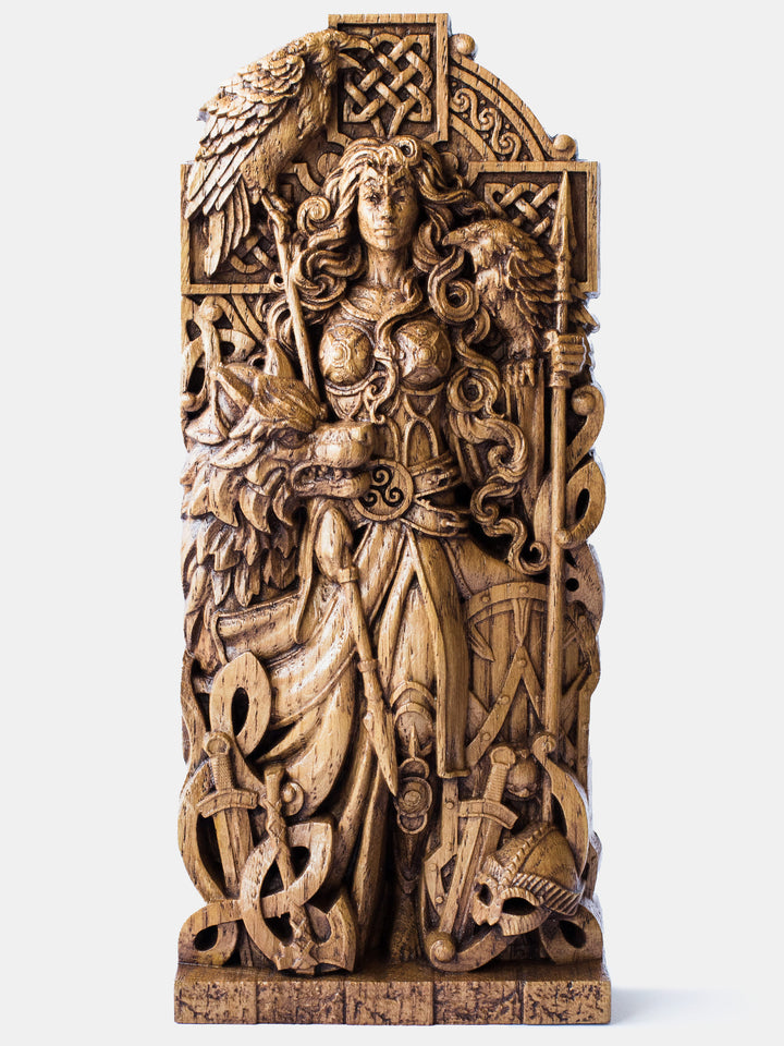 Close-up of the handcrafted oak Morrigan statue, showcasing the goddess holding two spears with a Celtic cross in the background, accompanied by two ravens and a wolf.