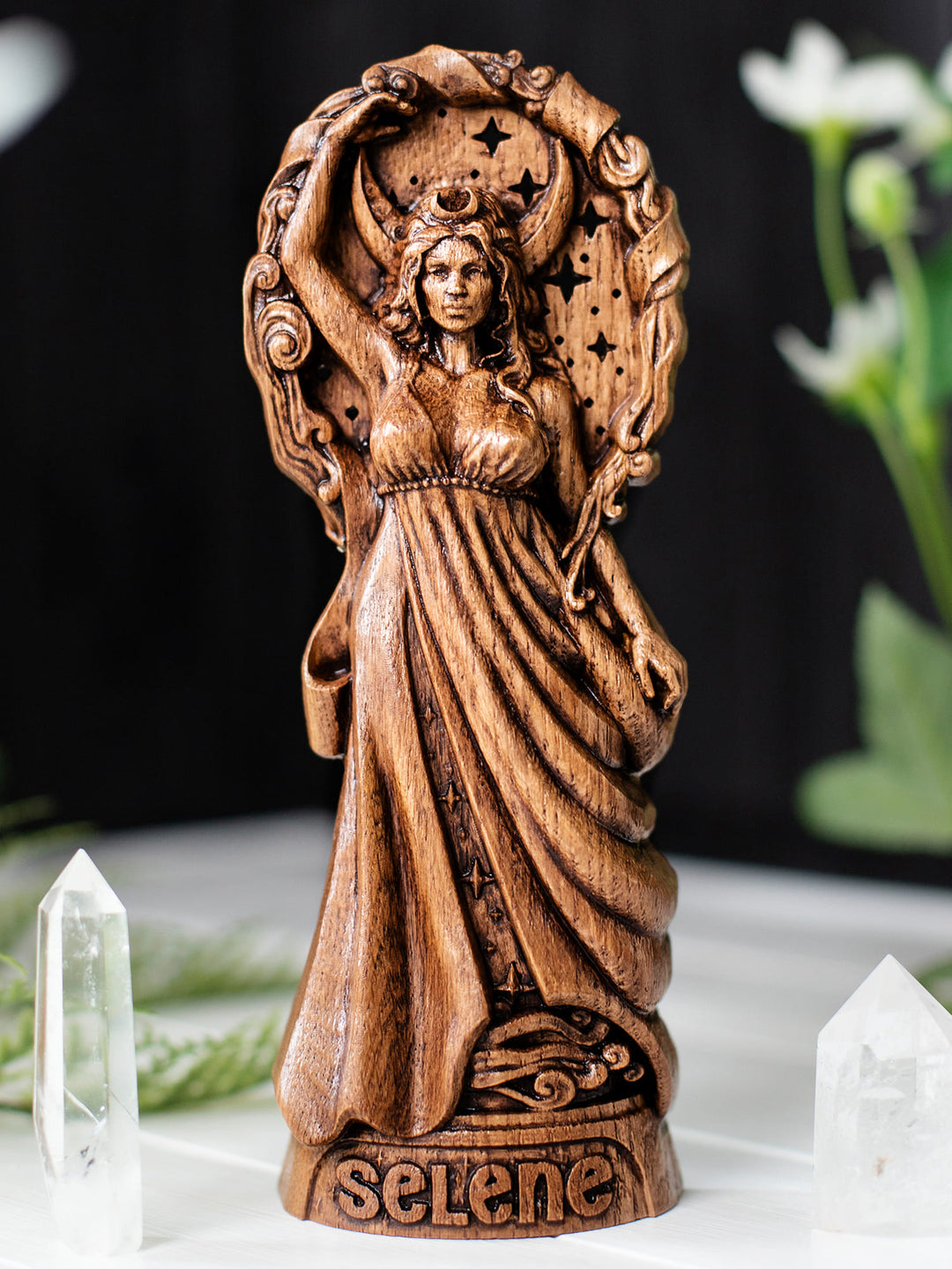 Wooden moon goddess Selene figurine with raised arm embracing starry night and lunar backdrop.