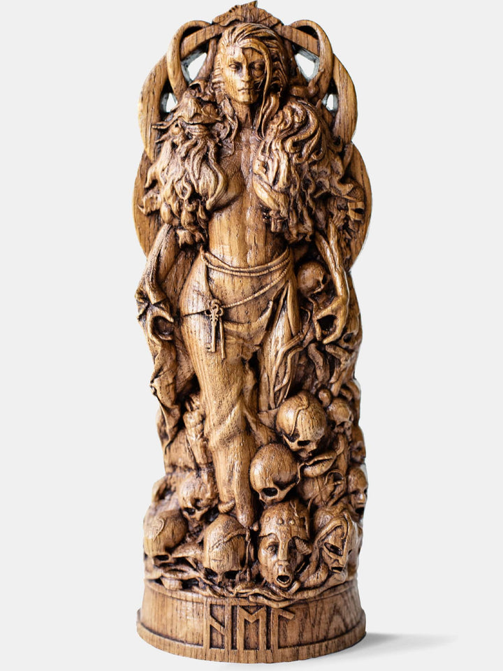 Close-up of the handcrafted oak Hel statue, showcasing her dual nature in a majestic pose with skulls and frightened faces at her feet.